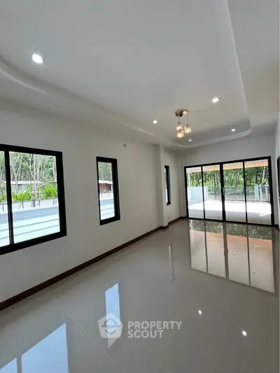 Spacious modern living room with large windows and glossy tile flooring, offering a serene view of lush greenery.