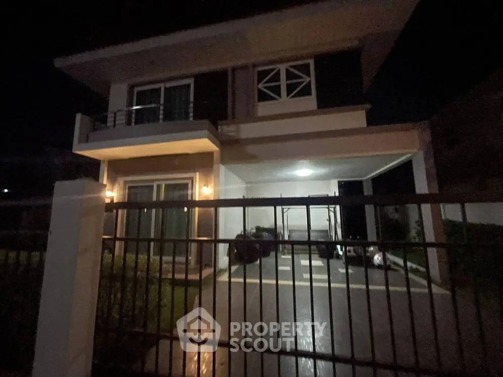 Modern two-story house with balcony and gated driveway at night