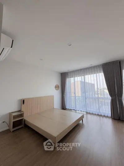 Spacious bedroom with large windows and modern minimalist design, featuring wooden flooring and a stylish bed frame.