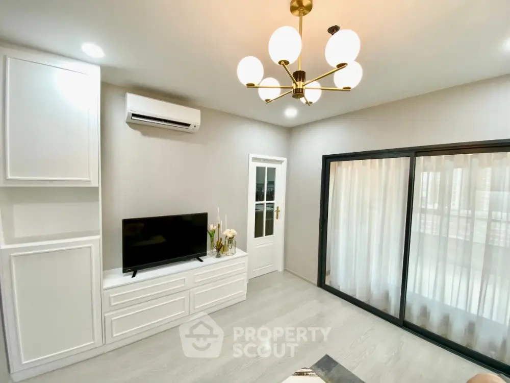 Elegant living room with modern gold chandelier, sleek white built-in cabinets, and large sliding glass doors leading to a bright, airy balcony.