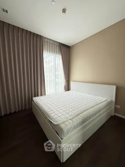 Spacious bedroom with large window and elegant curtains in modern apartment.