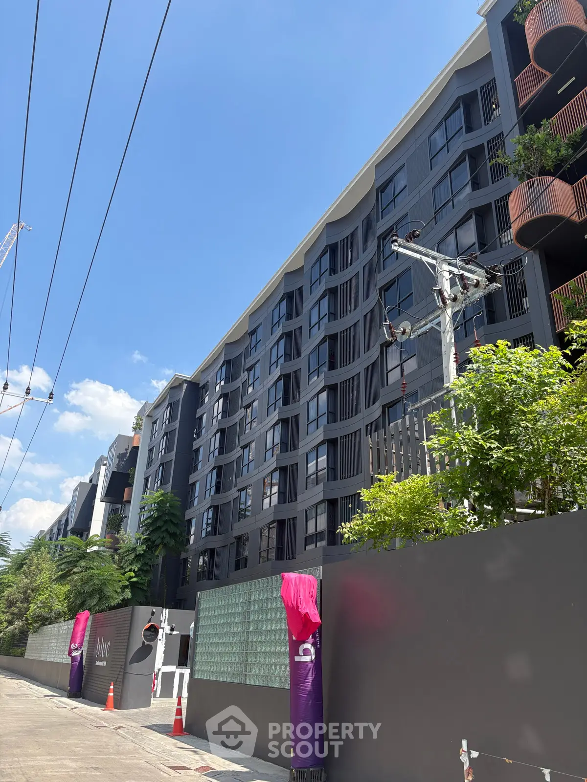 Modern apartment building exterior with lush greenery and clear blue sky.