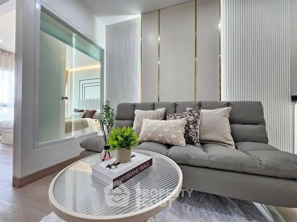 Modern living room with stylish sofa and glass partition leading to bedroom, featuring elegant decor and natural light.