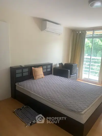 Spacious bedroom with large window and balcony access, featuring modern air conditioning and cozy seating area.