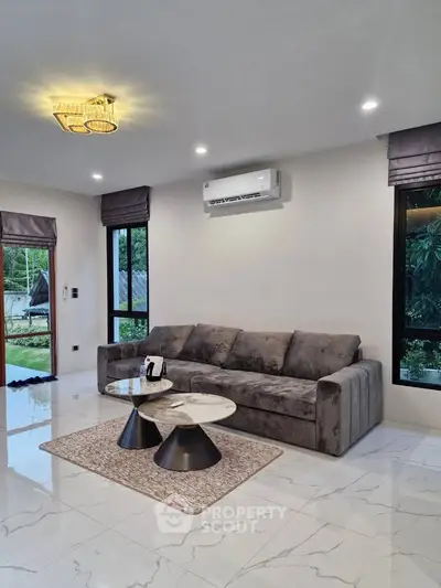 Modern living room with sleek gray sofa, stylish coffee tables, and large windows offering lush garden views.