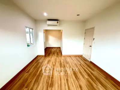 Spacious empty room with wooden flooring and air conditioning, perfect for customization.