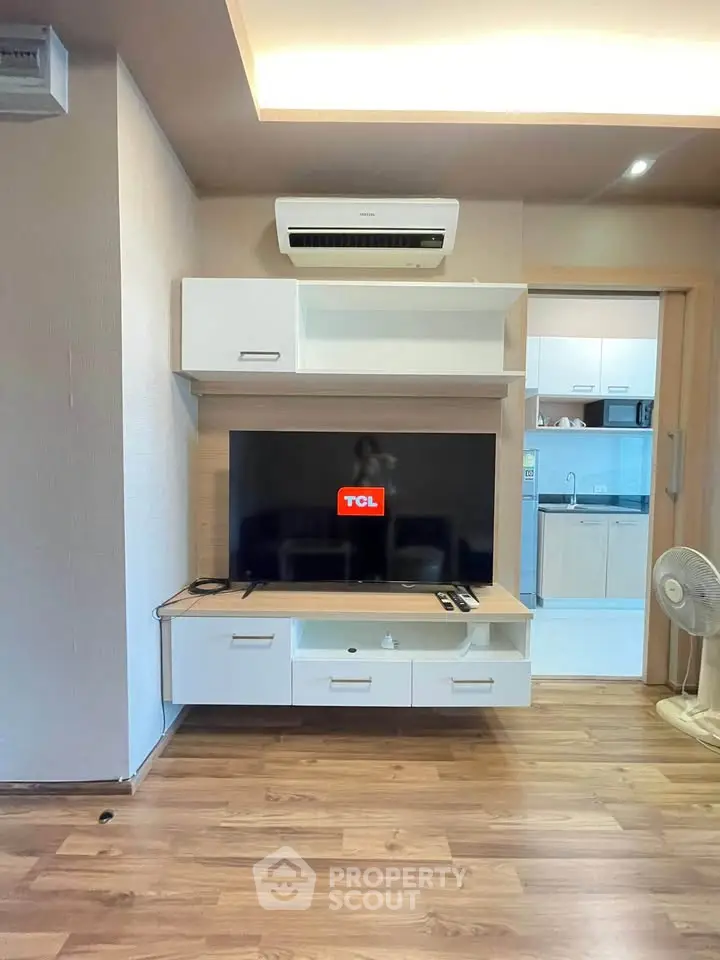 Modern living room with wall-mounted TV and air conditioning, featuring wooden flooring and open kitchen view.