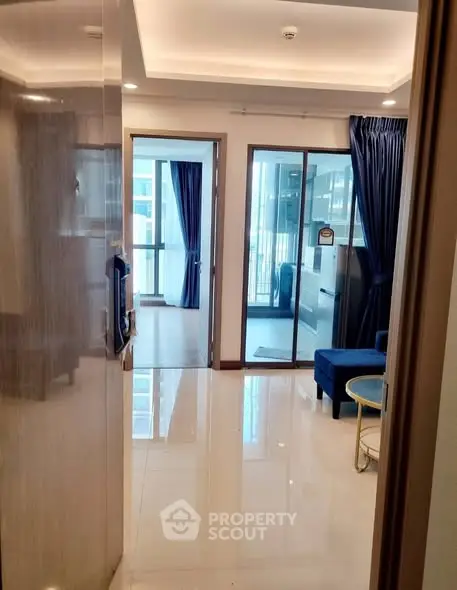 Modern apartment entrance with sleek flooring and glass doors leading to a bright living area.
