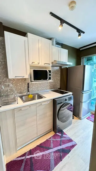 Modern kitchen with sleek appliances and stylish cabinetry, featuring a washing machine and stainless steel fridge.