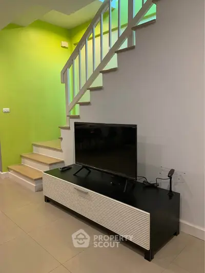 Modern living room with sleek TV stand and staircase, vibrant green accent wall, and stylish decor.