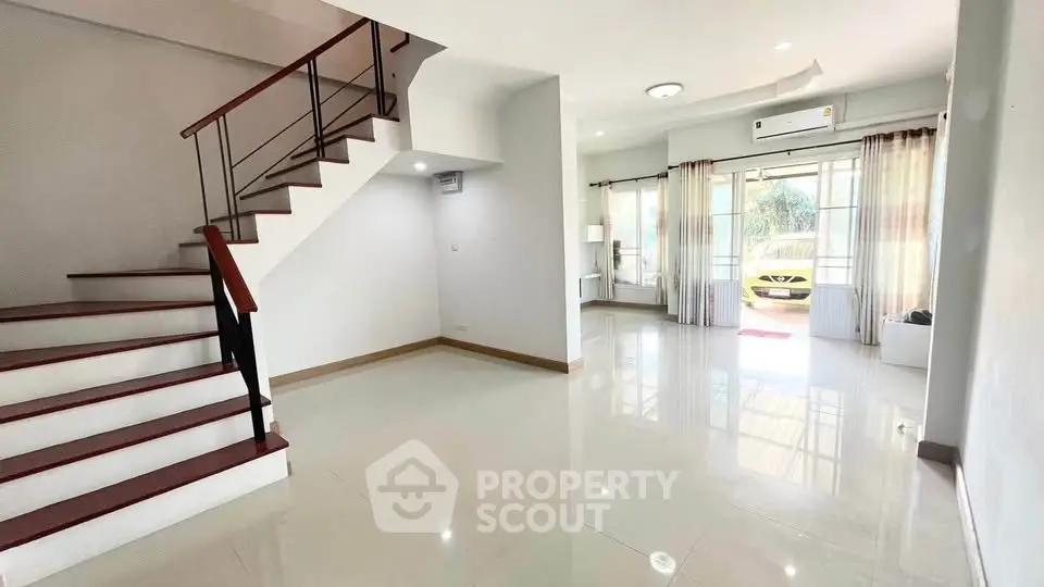 Spacious modern living room with staircase and large windows offering natural light.