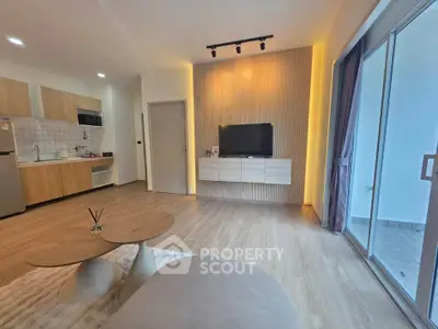 Modern living room with open kitchen and stylish decor, featuring a wall-mounted TV and large windows.