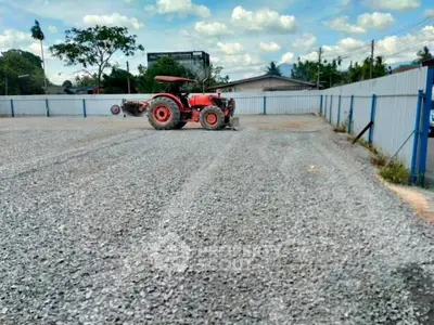 Spacious gravel lot with a tractor, ideal for development or storage, surrounded by fencing under a clear sky.