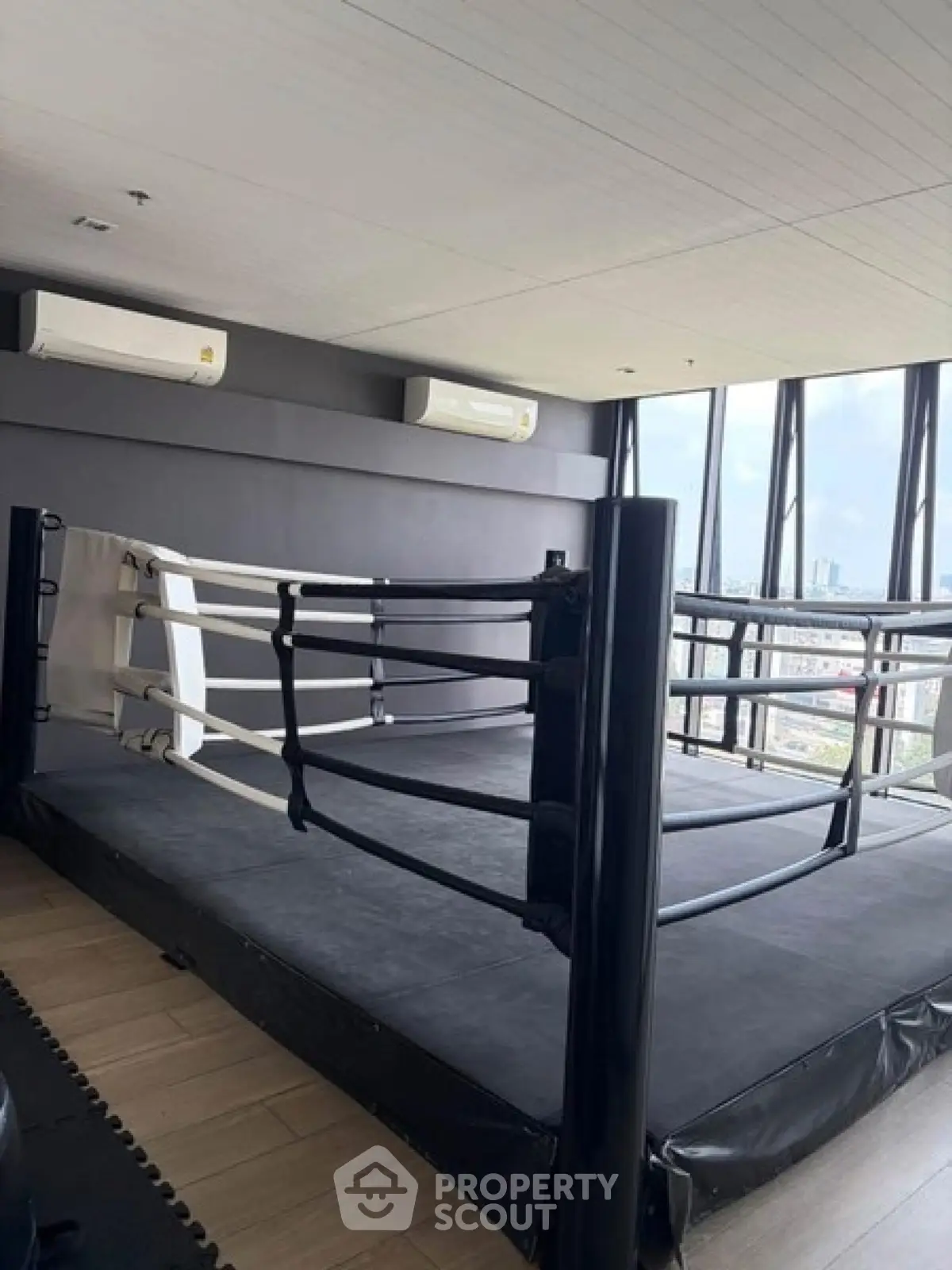 Spacious gym with boxing ring and panoramic city views, perfect for fitness enthusiasts.