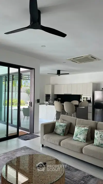 Modern open-layout living room with sleek kitchen and large glass doors leading to a patio.