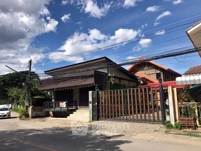 Charming traditional-style house with wooden facade and gated entrance under a vibrant blue sky.