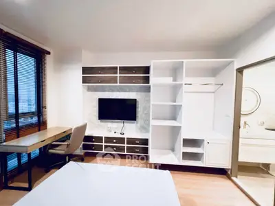Modern bedroom with built-in storage and workspace, featuring a wall-mounted TV and large window with blinds.