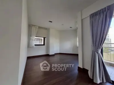 Spacious empty room with hardwood floors and large windows, perfect for customization.