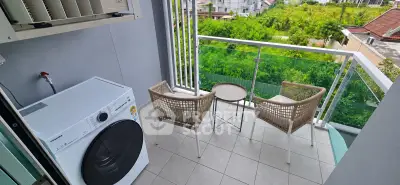 Charming balcony with lush green view, featuring cozy seating and modern washing machine.