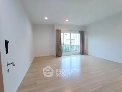 Spacious empty room with large window and wooden flooring, perfect for customization.