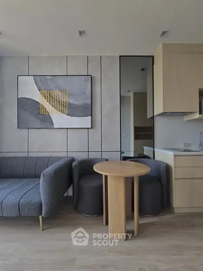 Modern living room with stylish furniture and abstract art, featuring a cozy seating area and sleek kitchen.