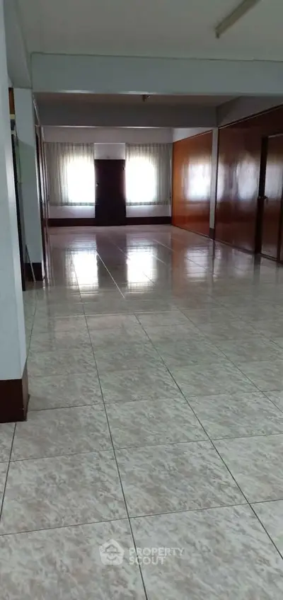 Spacious hallway with tiled flooring and large windows in a residential building.