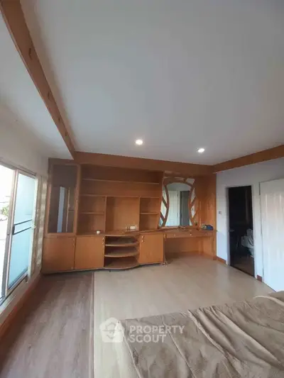 Spacious bedroom with built-in wooden shelves and large windows for natural light.