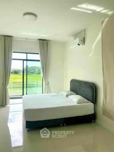 Bright bedroom with large window and scenic view of greenery.