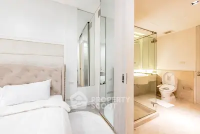 Modern bedroom with ensuite bathroom featuring glass shower and elegant decor.