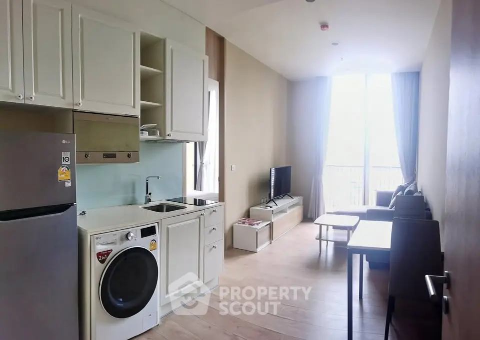 Modern open-layout living room with kitchen, featuring sleek appliances and natural light from large windows.