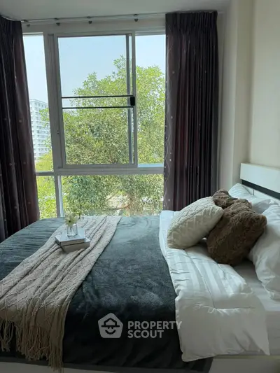 Cozy bedroom with large window and lush green view, featuring elegant bedding and decorative pillows.