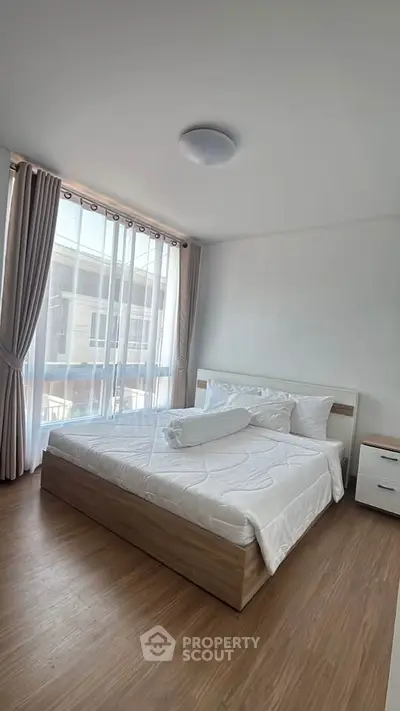 Spacious bedroom with large window and modern furnishings in a bright apartment.