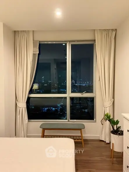 Cozy bedroom with large window offering stunning city night view, elegant curtains, and stylish decor.
