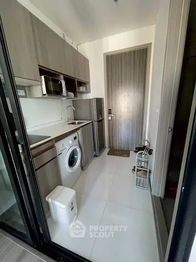 Modern compact kitchen with washing machine and microwave in sleek apartment.