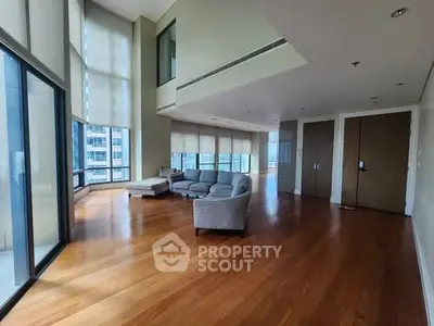 Spacious modern living room with floor-to-ceiling windows and wooden flooring in a high-rise apartment.