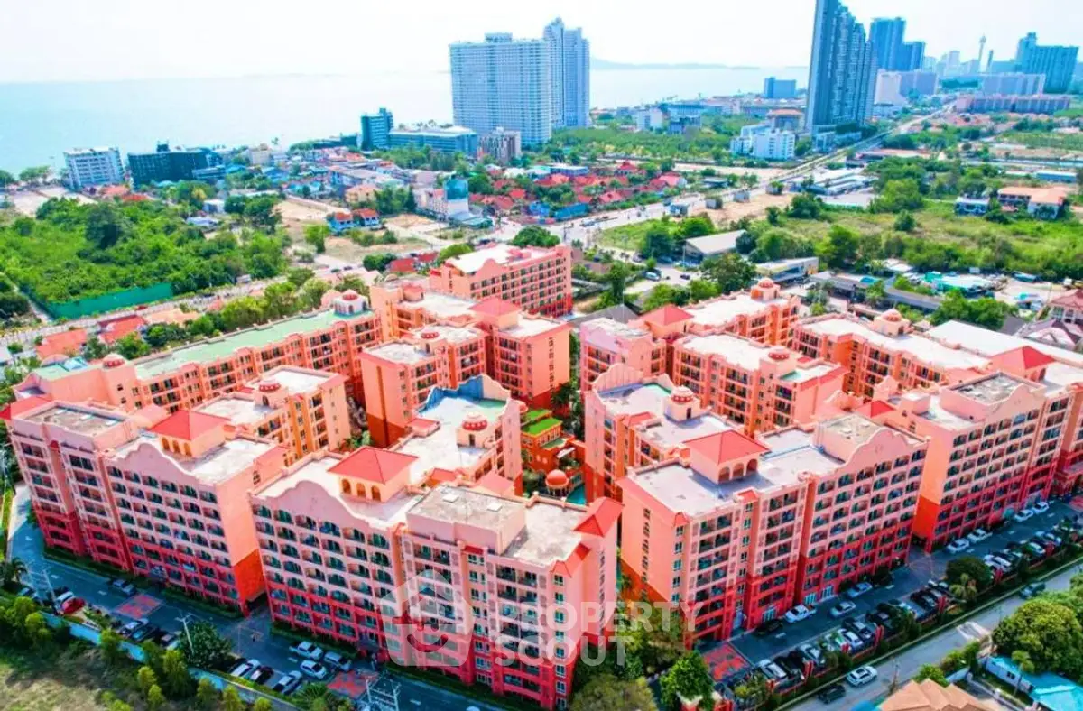 Aerial view of vibrant pink residential complex with ocean backdrop and city skyline.