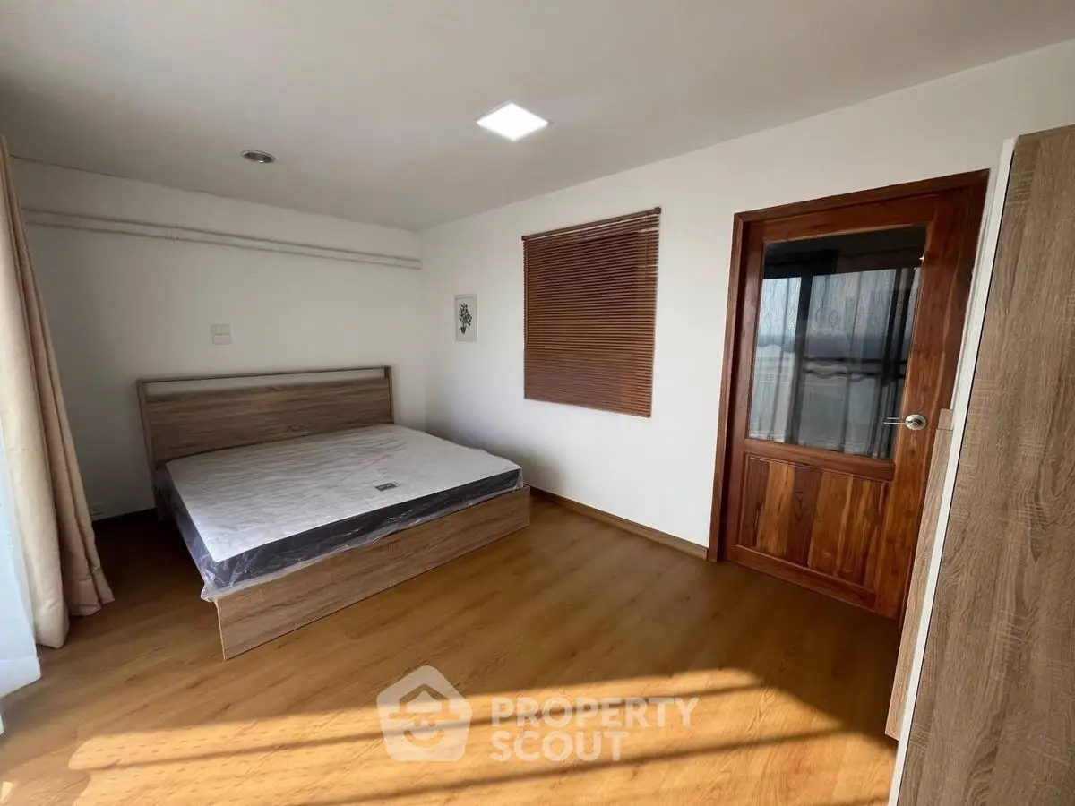 Spacious bedroom with wooden flooring and modern design, featuring a large window for natural light.