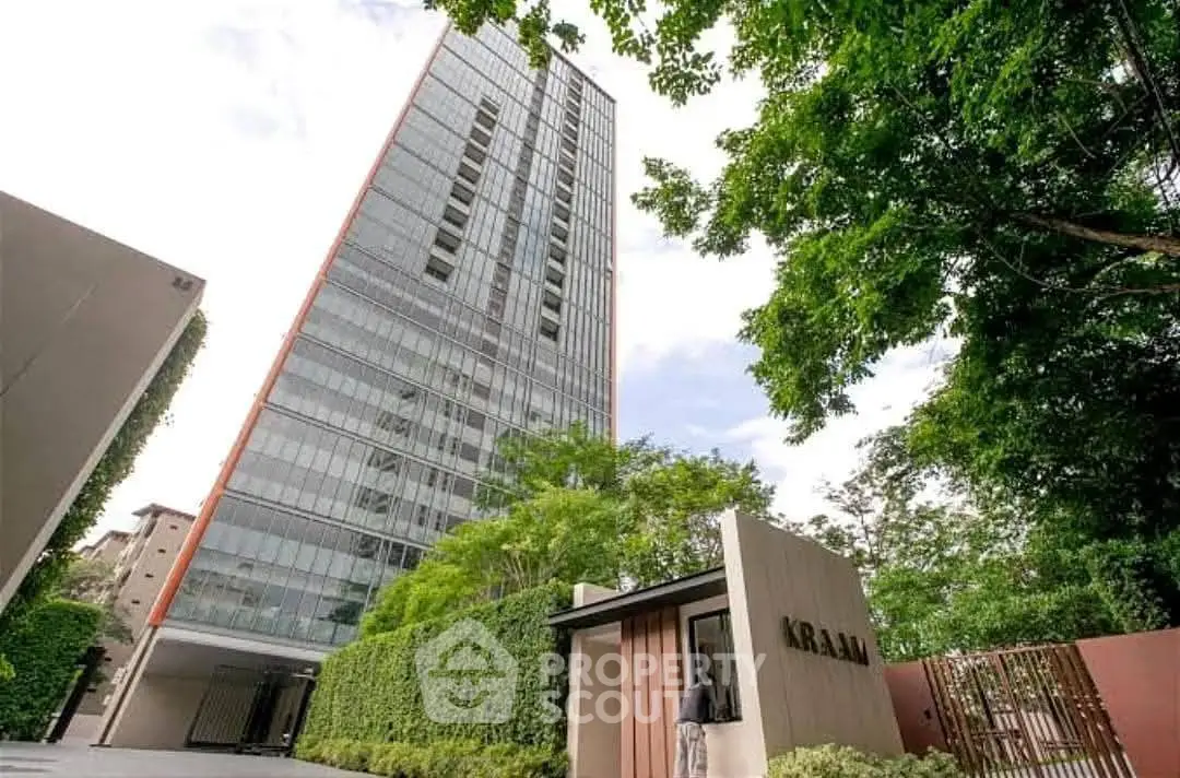 Modern high-rise building with lush greenery and secure entrance in urban setting.