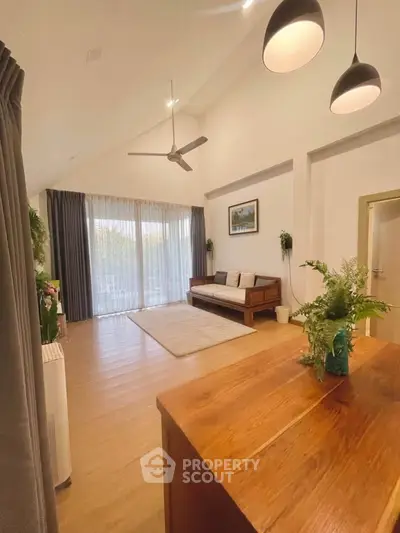 Spacious living room with high ceiling, wooden flooring, and large windows offering natural light.