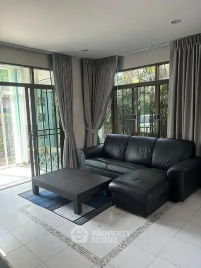 Spacious living room with modern black leather sofa and large windows for natural light.