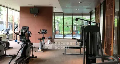 Spacious gym with modern equipment and large windows overlooking greenery