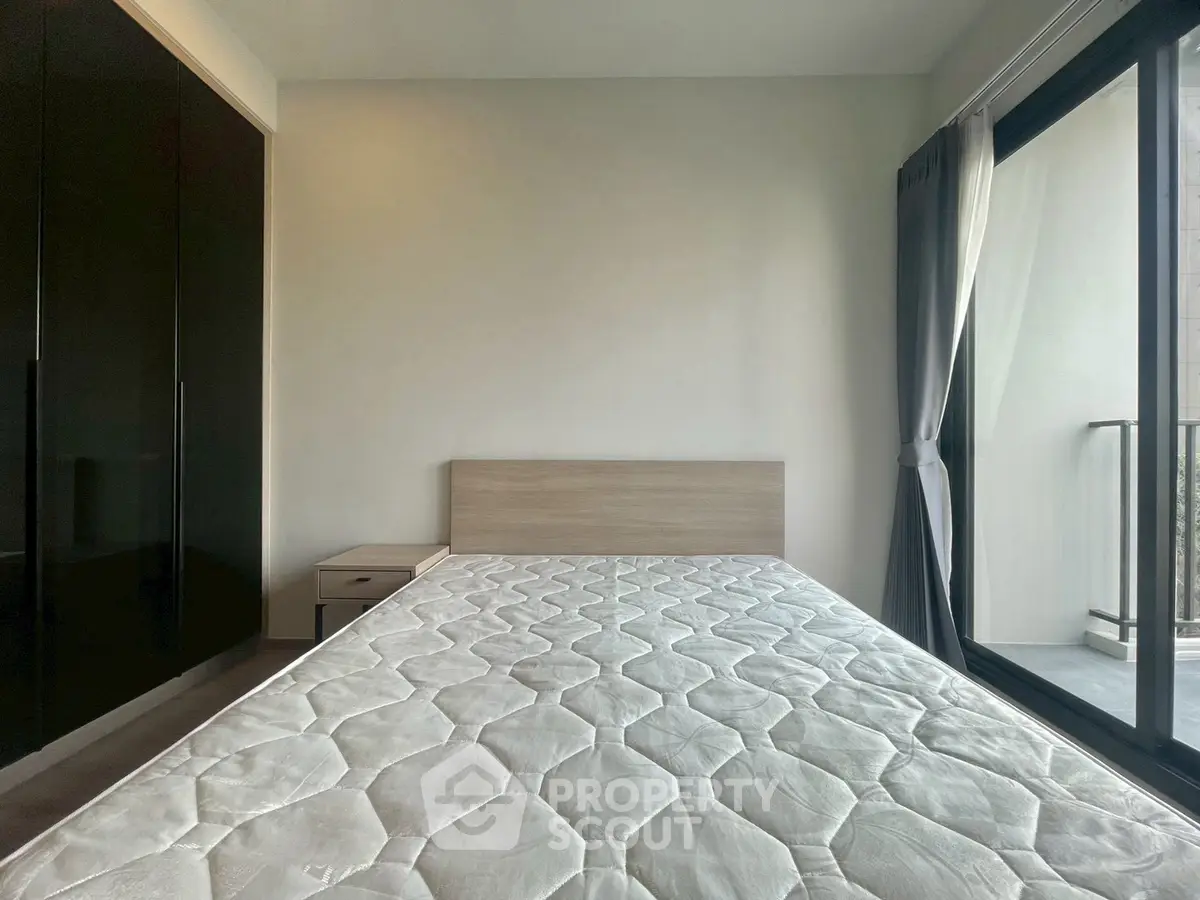 Modern bedroom with large window and balcony access, featuring sleek black wardrobe and minimalist design.