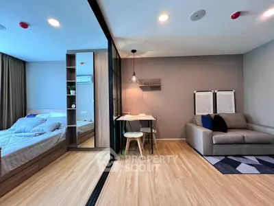 Modern studio apartment with cozy living area and stylish bedroom separated by glass partition.