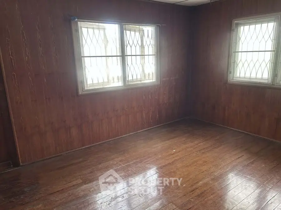 Spacious empty room with wooden walls and floor, featuring barred windows.