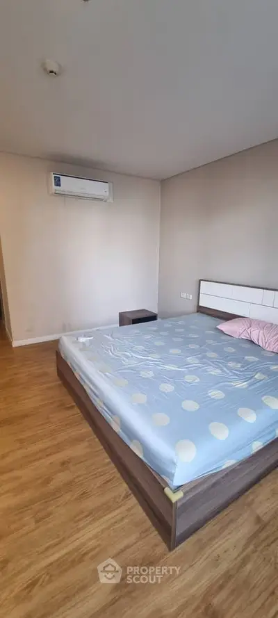 Spacious bedroom with wooden flooring and air conditioning, featuring a modern bed setup.