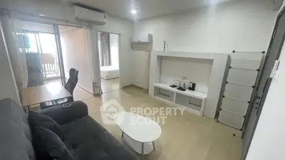 Modern living room with sleek furniture and open layout leading to a bedroom, featuring natural light.