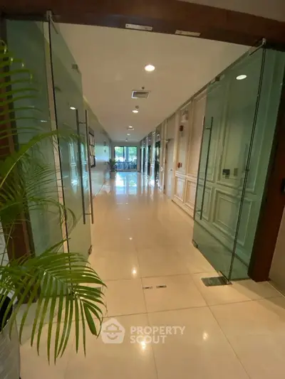Elegant office corridor with glass doors and polished floors, leading to a bright meeting area.
