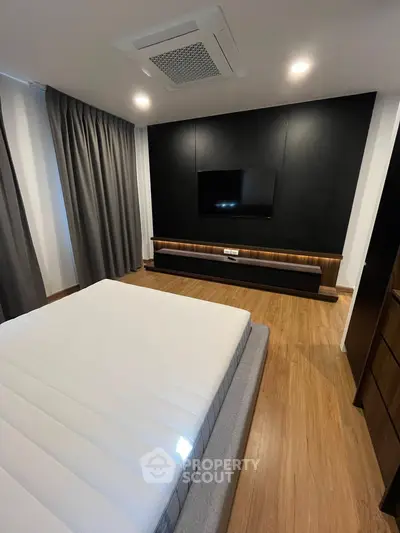 Modern bedroom with sleek design, featuring a wall-mounted TV and elegant wood flooring.