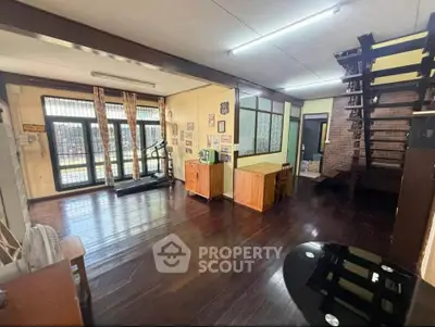 Spacious living room with wooden floors and modern decor, featuring a treadmill and stylish staircase.