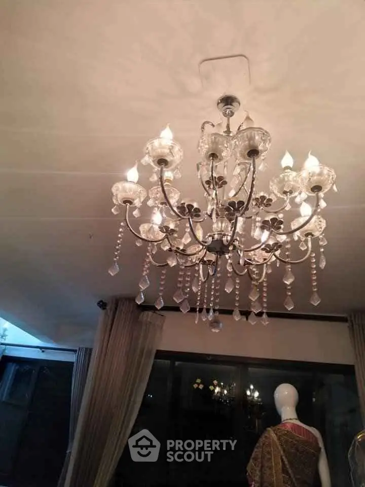 Elegant chandelier in a stylish living room with large windows and luxurious curtains.